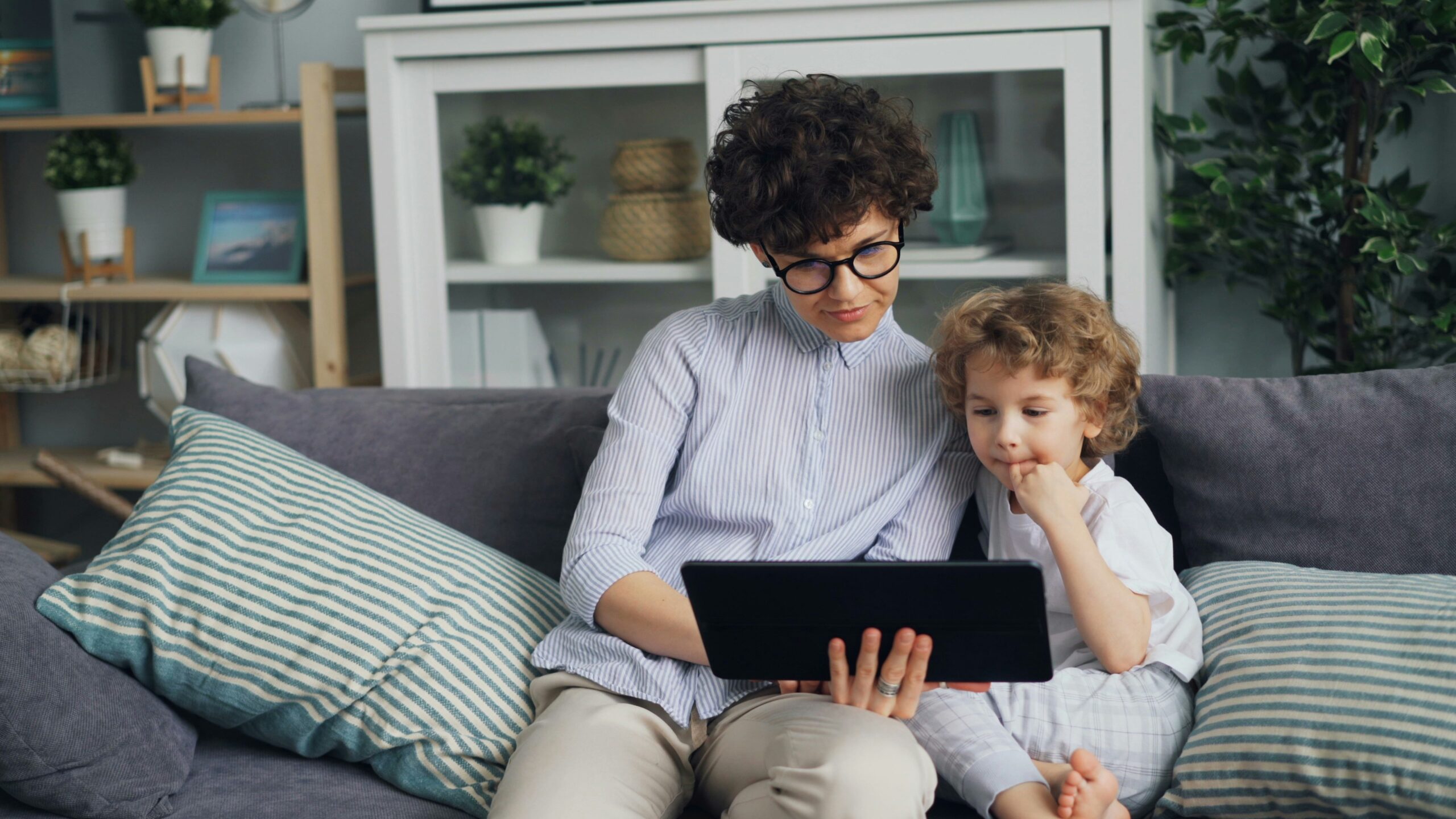 Kind sitzt mit Tablet auf dem Sofa